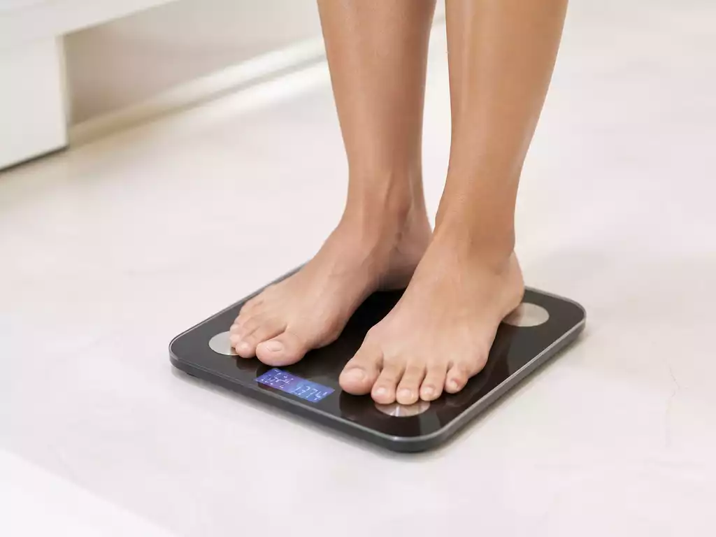 Person using a digital scale to check their weight, with the display showing both kg and lbs units