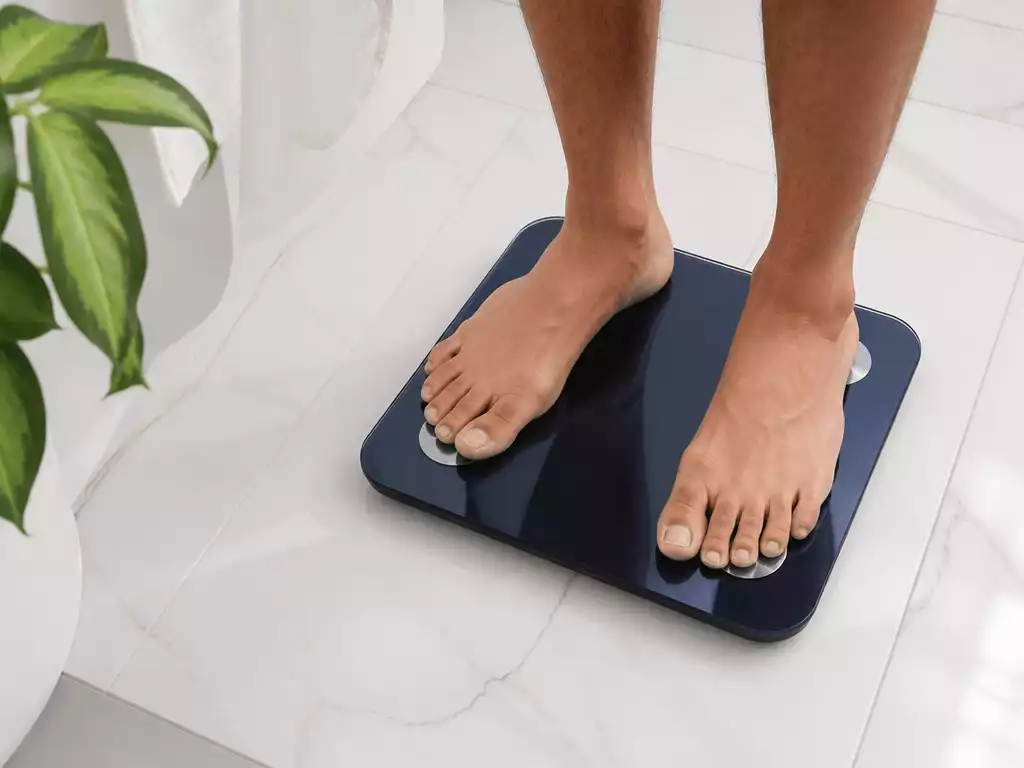 Modern Wyze Scale on a clean bathroom floor with a person's feet visible, indicating usage