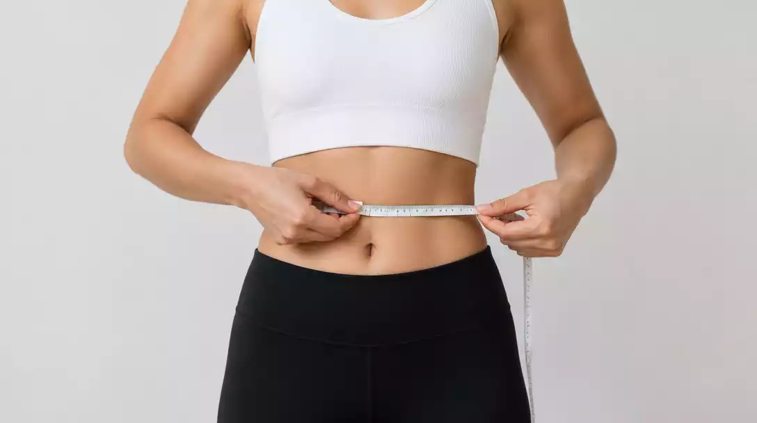Person using a tape measure around their waist, demonstrating proper technique for waist measurement.