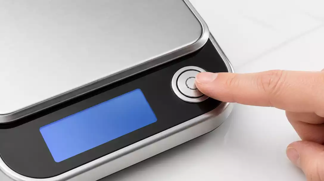 Hand pressing a reset button on a digital kitchen scale