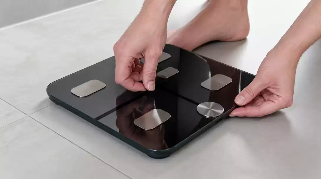 Person resetting a modern digital bathroom scale on a clean bathroom floor